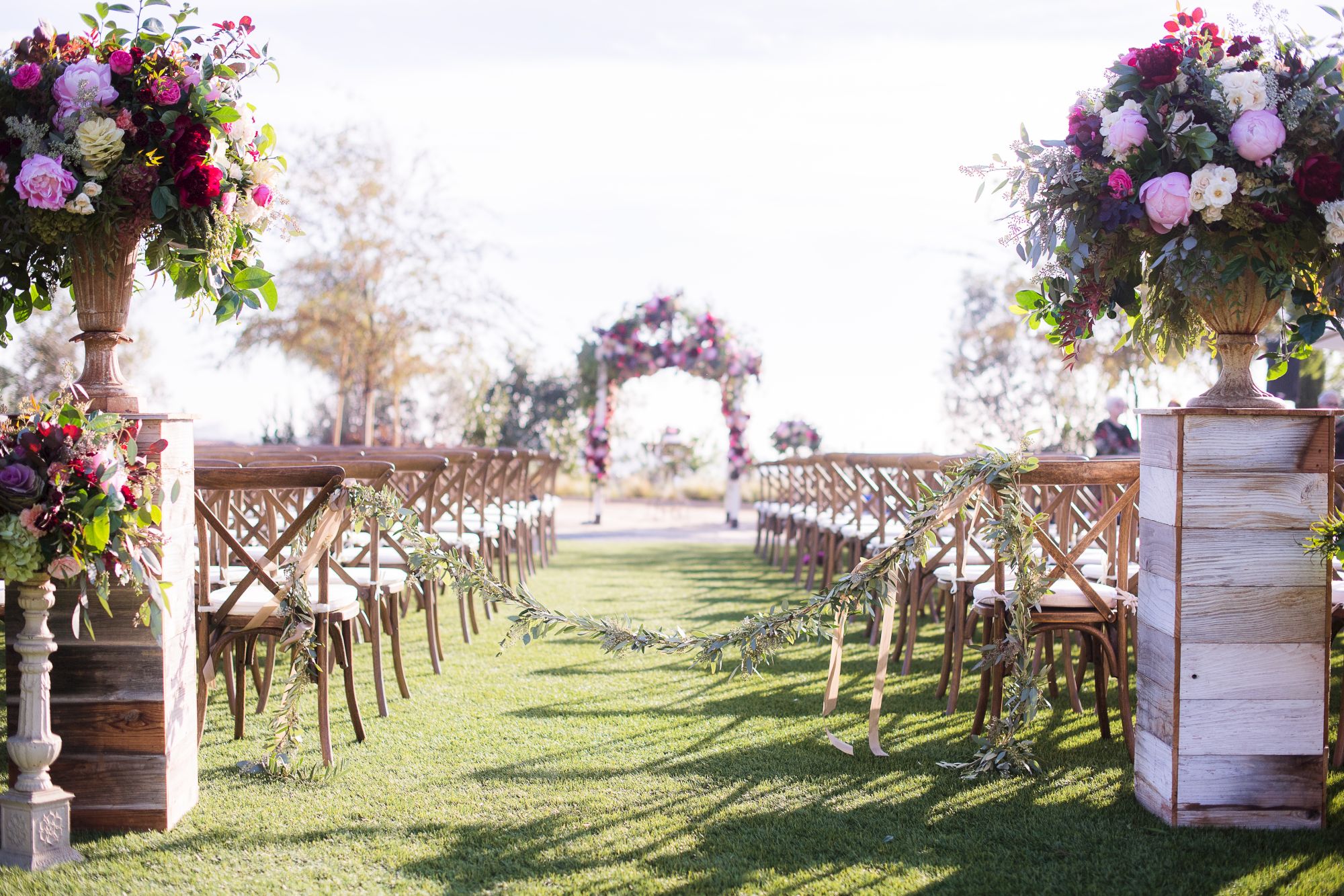 Beautiful outdoor wedding aisle with wooden chairs, floral arches, and lush bouquets lining the ceremony path.