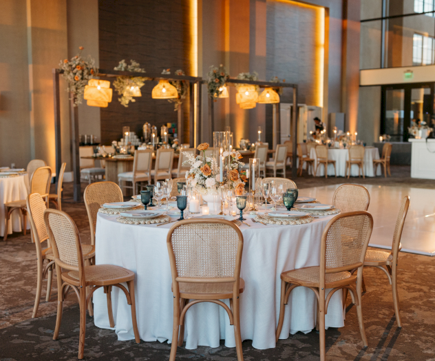 An elegant restaurant with white-draped tables, wooden chairs, warm lighting, and a cozy, upscale dining vibe.