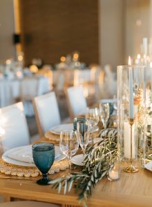 A warmly lit table set for a formal event with wine glasses, candles, and greenery centerpiece, ready for guests.