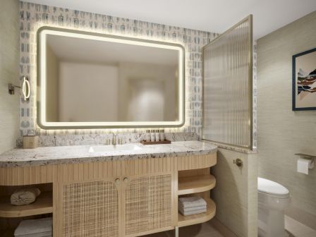 A modern bathroom with a backlit mirror, woven cabinet, open shelves, beige tones, patterned wall tile, and a sleek toilet beside the door.