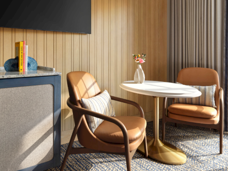 A stylish cozy sitting area with two tan leather chairs around a white round table, a blue cabinet, wooden paneled wall, and a sliding glass door blending indoor/outdoor vibes.