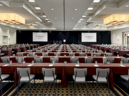 A large conference room set up with rows of tables and chairs, red tablecloths, and a stage with screens and podiums for a formal event.