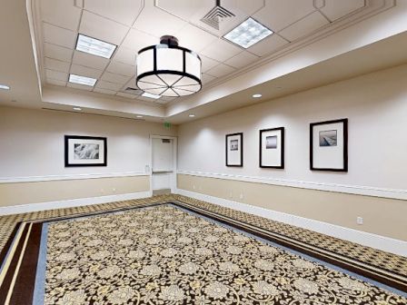 A spacious, well-lit conference room with patterned carpet, framed black-and-white photos on cream walls, and a large modern chandelier hanging from a coffered ceiling.