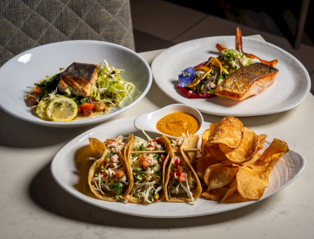 Delicious plate trio: spicy tuna tacos topped with creamy sauce, a side of fresh greens, and crispy tortilla chips with salsa.