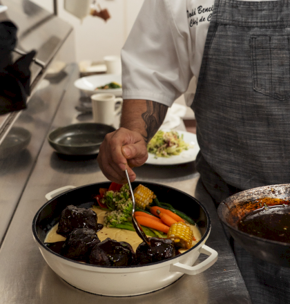 A chef stirs colorful vegetables in a sizzling pan on a stovetop, preparing a vibrant dish at a busy kitchen.