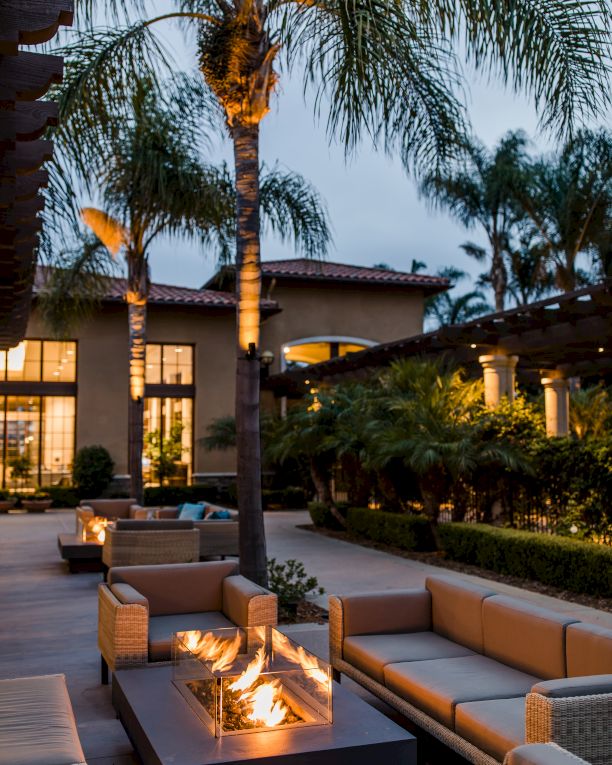 A modern outdoor lounge area with fire pit, palm trees, and courtyard seating at twilight.