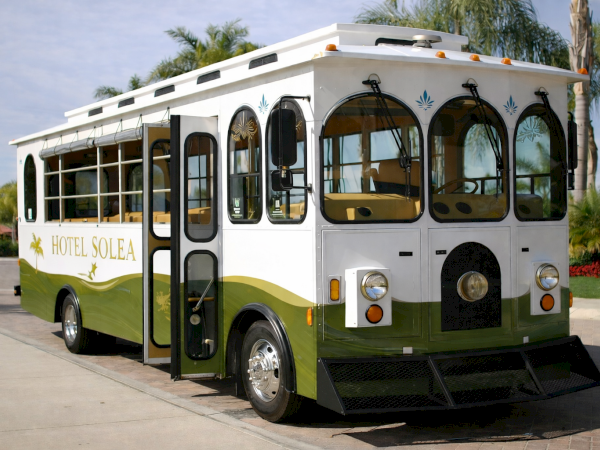 A vintage hotel shuttle bus named &ldquo;Hotel Solea,&rdquo; white with green trim, open-air front seating, parked on a sunny driveway.