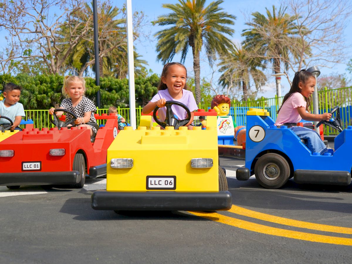 Kids are driving colorful bumper cars on a sunny day at an amusement park, smiling and racing ahead.