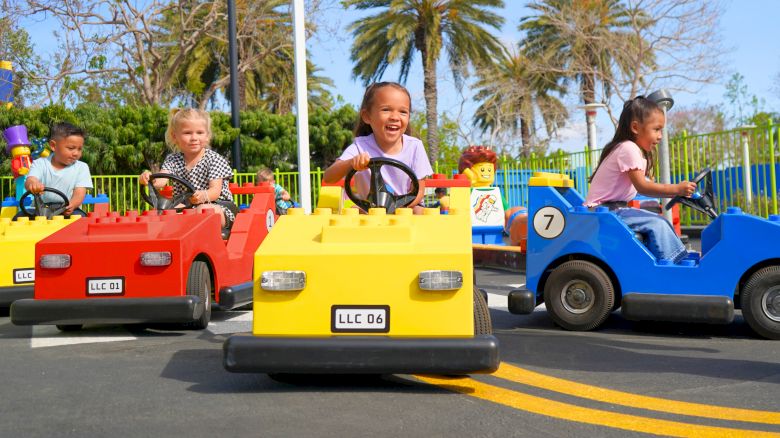 Kids are driving colorful bumper cars on a sunny day at an amusement park, smiling and racing ahead.